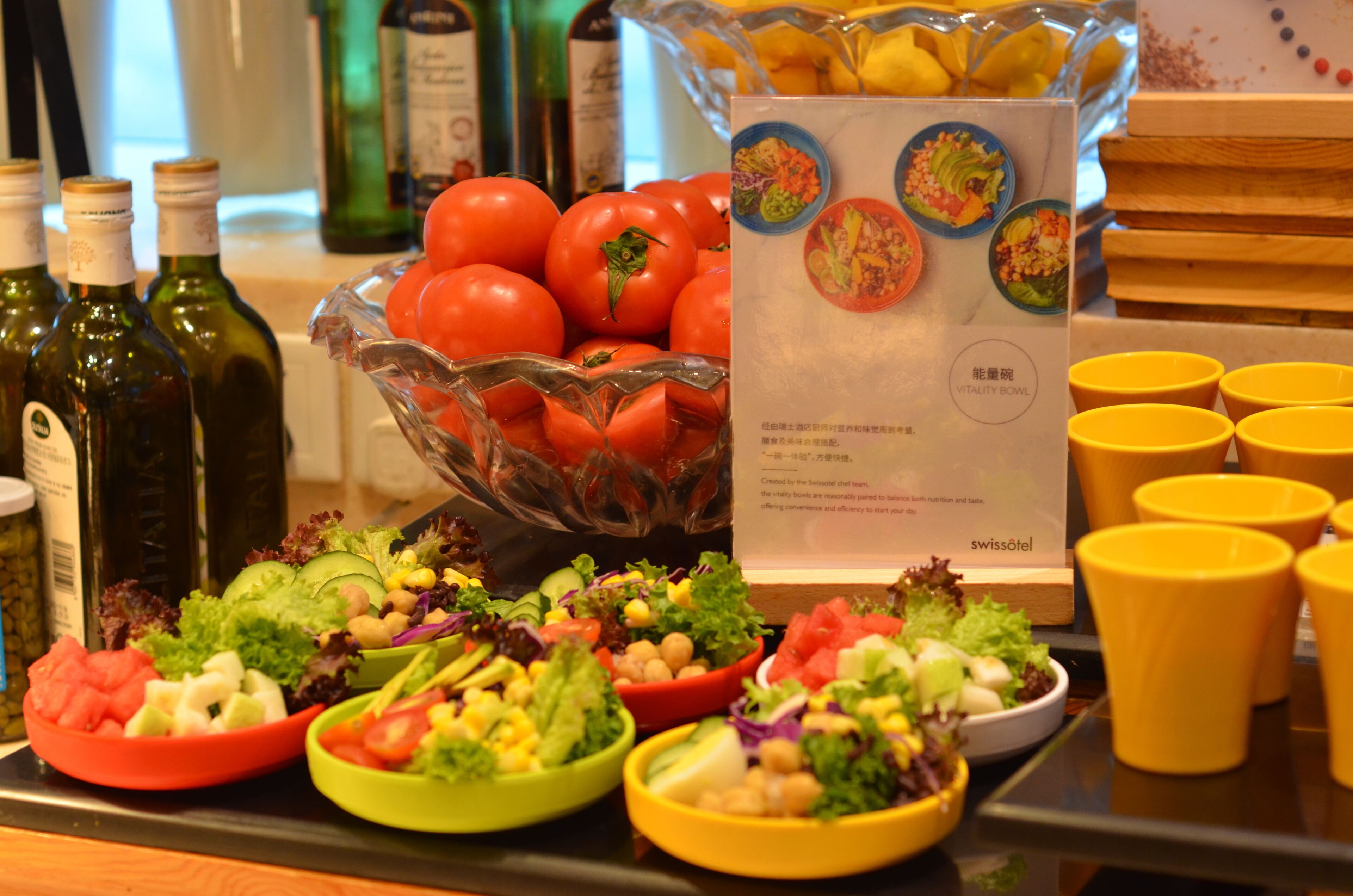 A buffet table with various salads, a bowl of tomatoes, and several bottles of olive oil.