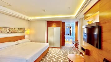 A hotel room with a large bed, a TV, a desk, and a bathroom visible through an open door.
