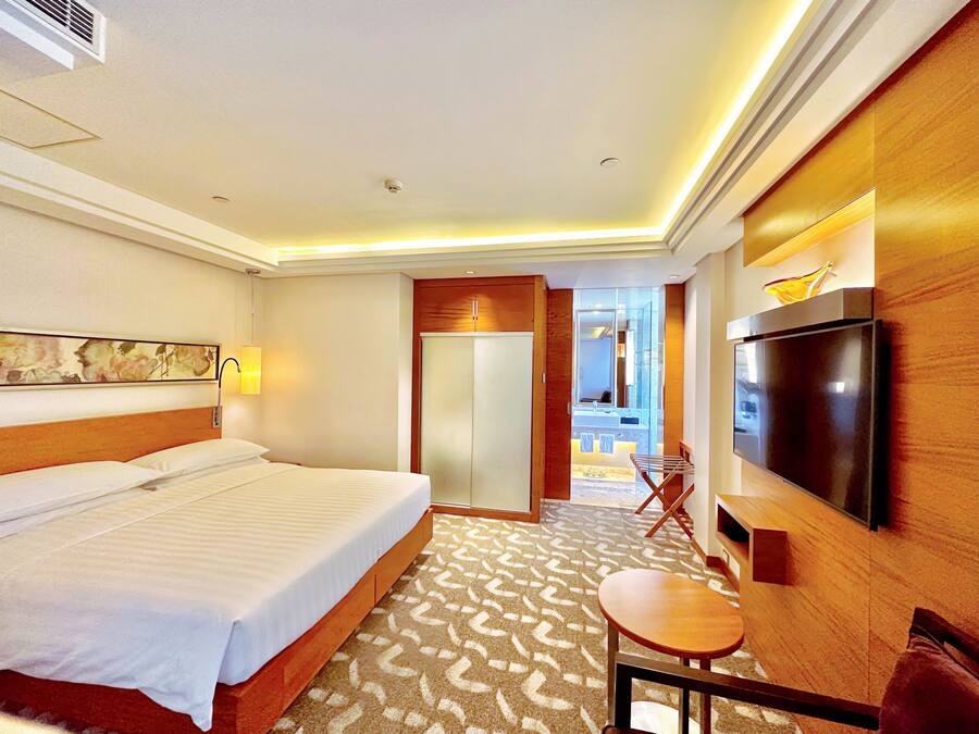 A hotel room with a large bed, a TV, a desk, and a bathroom visible through an open door.