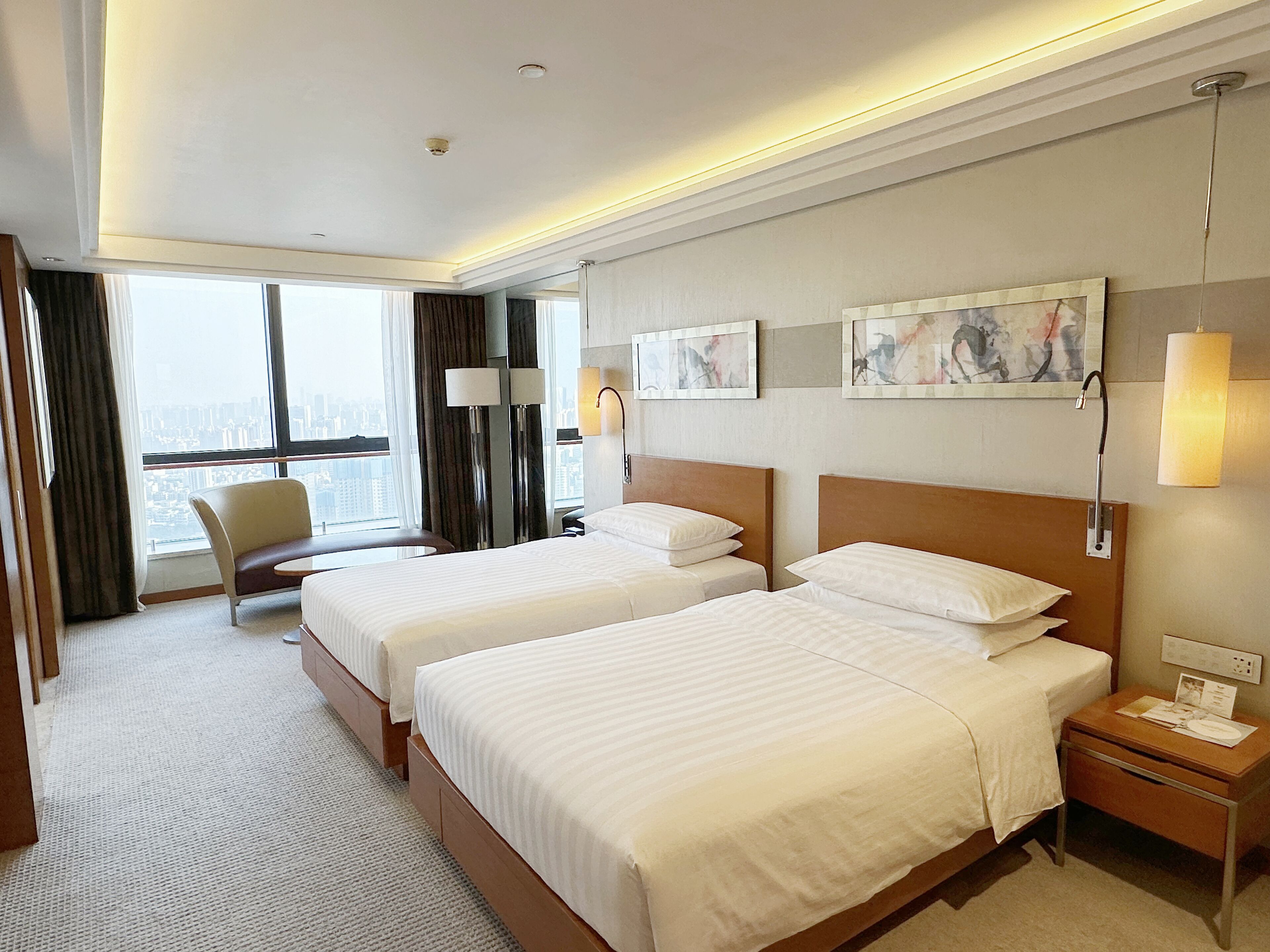 Une chambre d’hôtel avec deux lits, un bureau, une chaise et une grande fenêtre donnant sur la ville.
