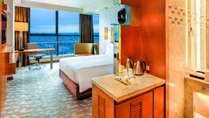 A hotel room with a large bed, a desk, a chair, a view of the city, and a bathroom with a mirror and sink. - Swissotel Foshan (Foshan)