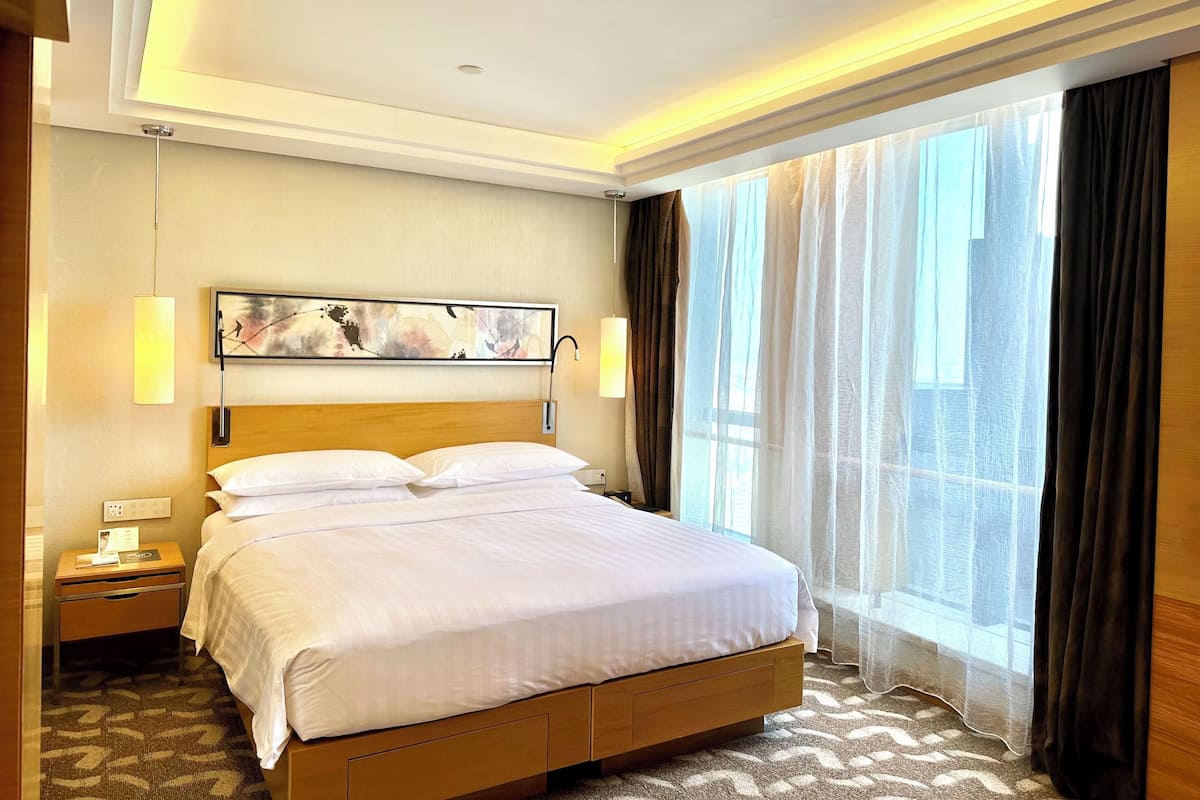 Habitación de hotel con una cama grande, una mesita de noche, una obra de arte colgada en la pared y una ventana con cortinas.