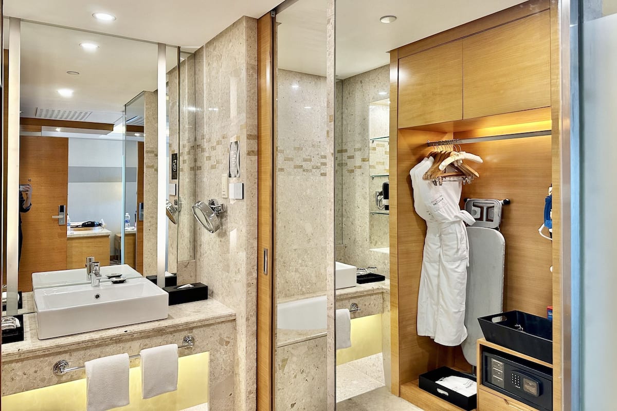 Un baño moderno con un espejo grande, un lavabo y una ducha. Hay un mueble de tocador de madera con un perchero y un armario negro.