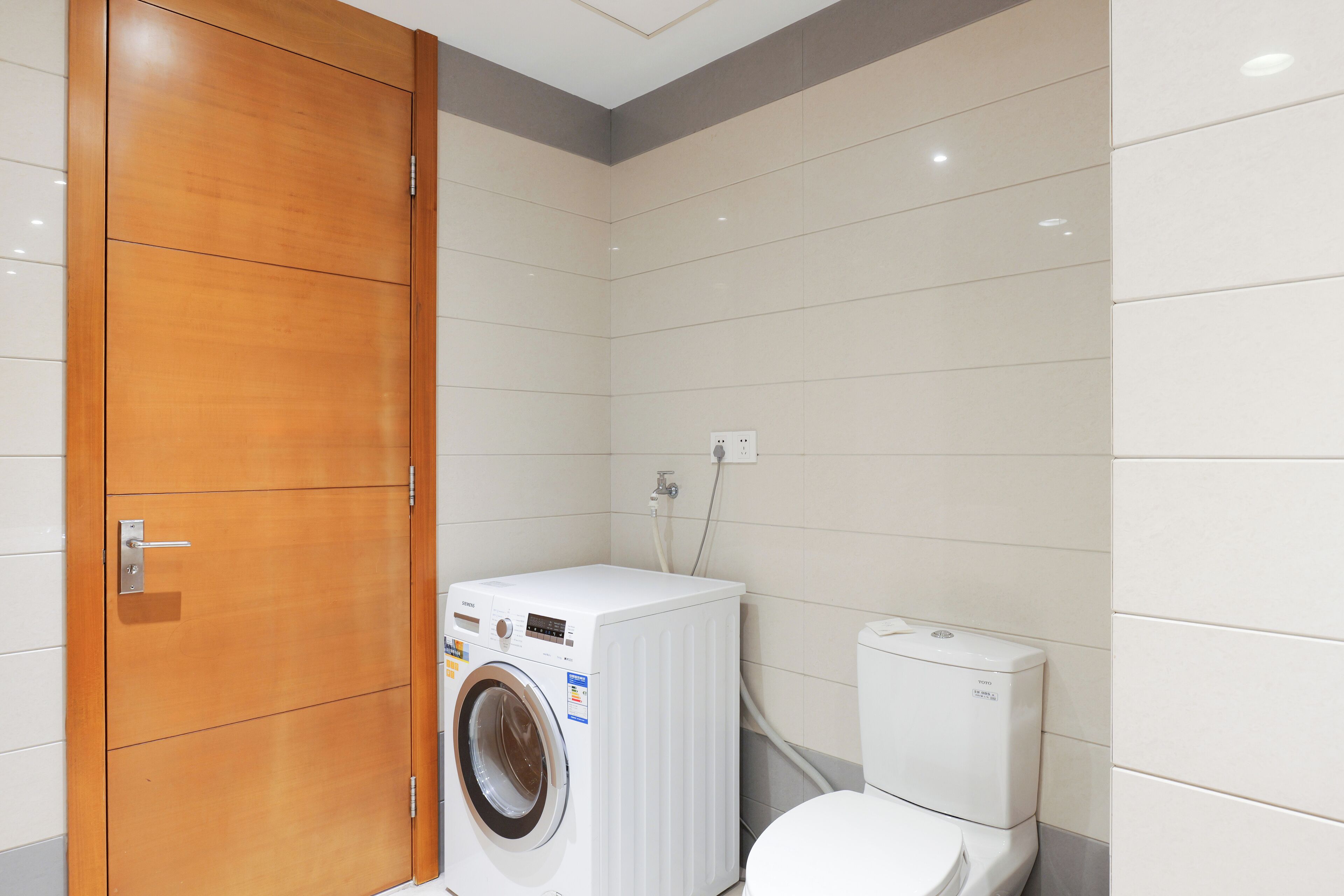 A compact bathroom with a wooden door, a white washing machine, and a toilet.