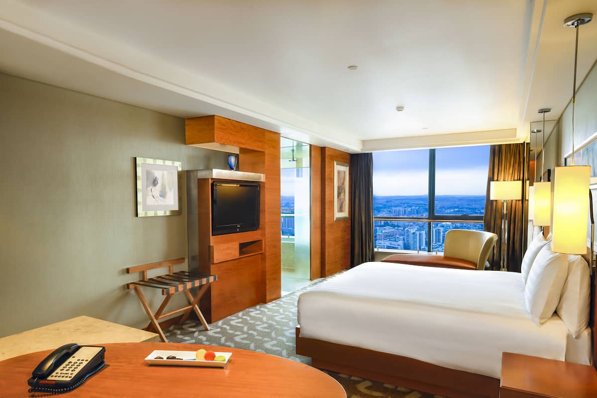 Una habitación de hotel con cama, escritorio, silla, televisor y vista a la ciudad.