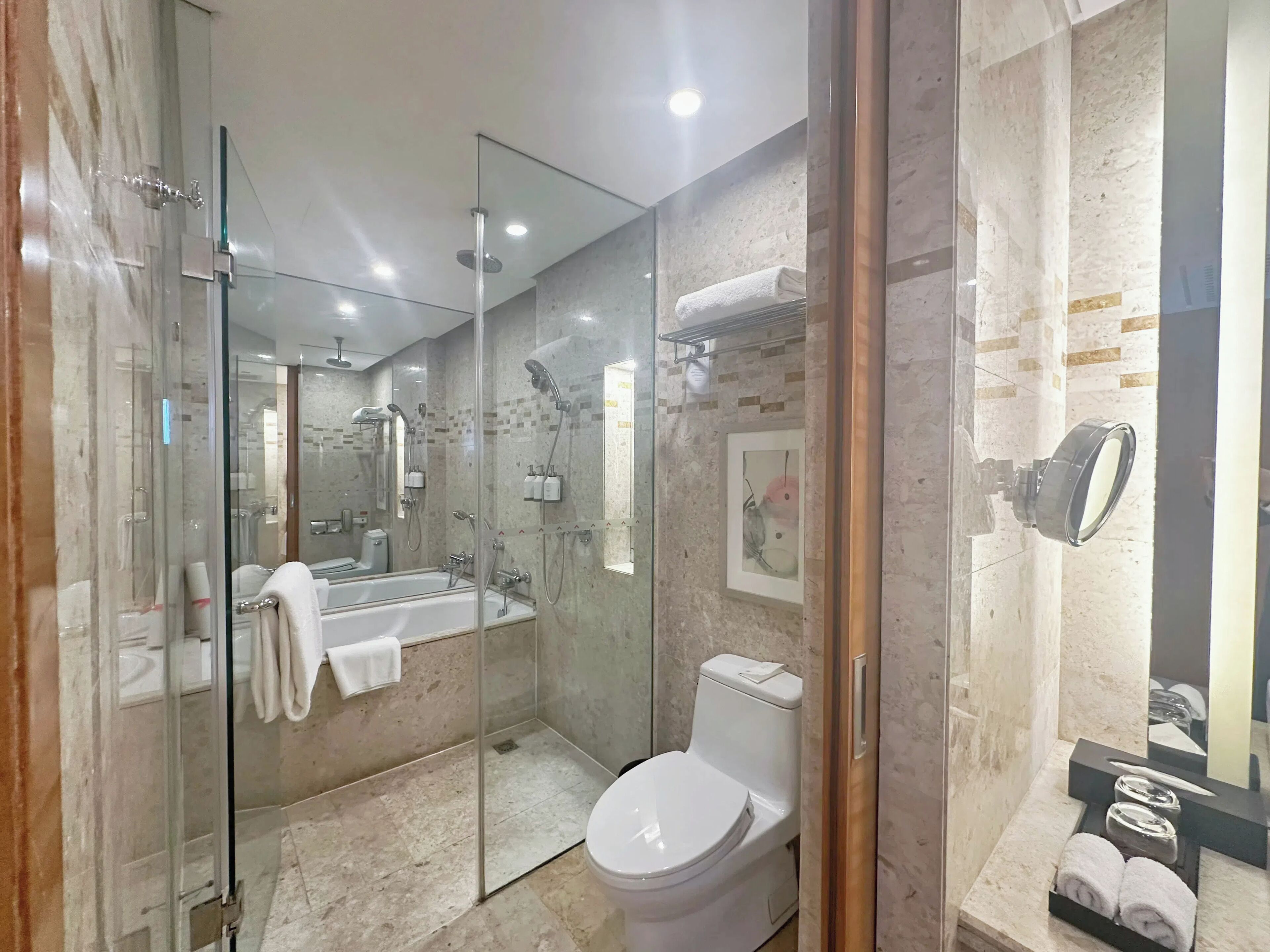Un baño moderno con ducha de vidrio, un espejo grande, una bañera y un inodoro.