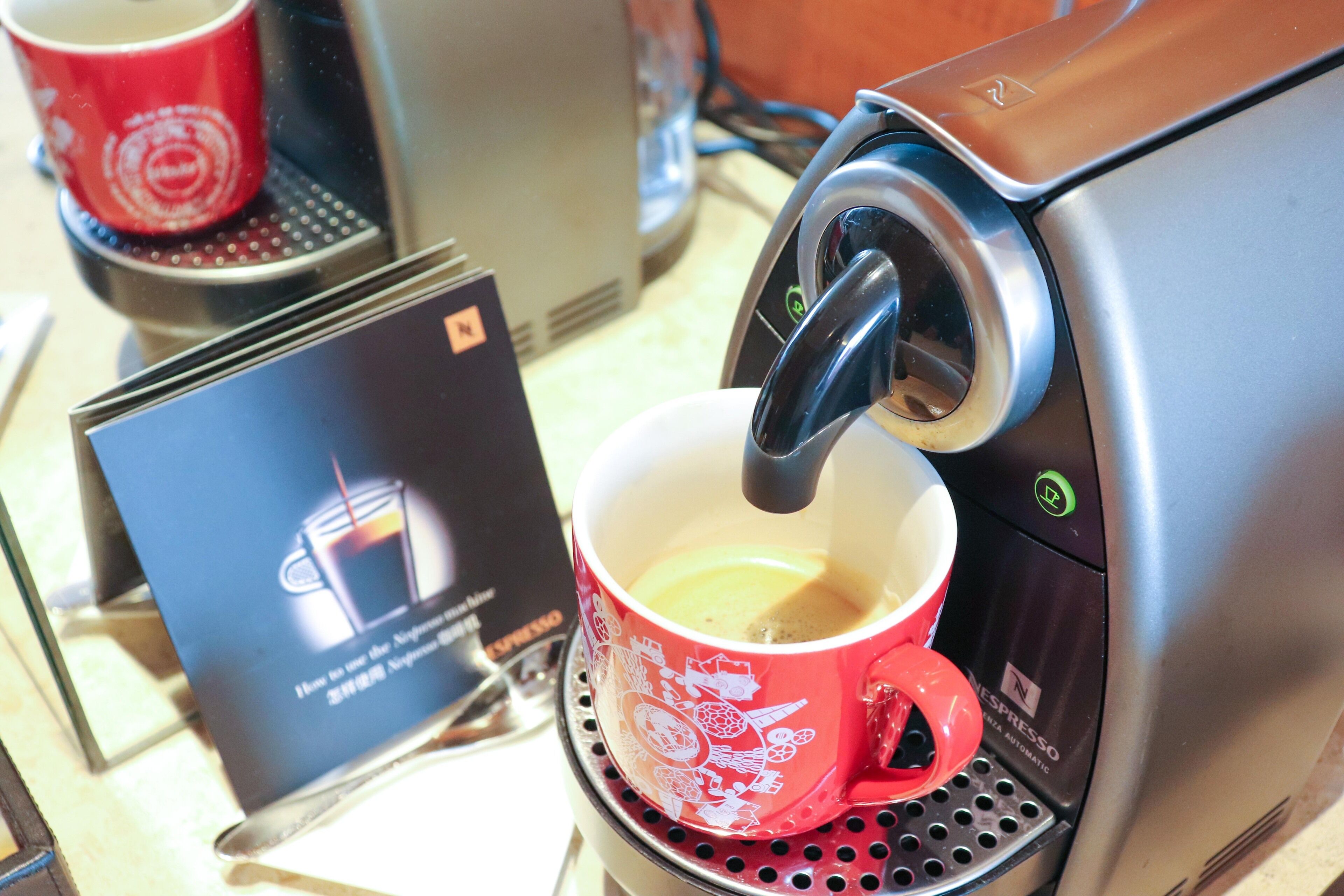 En kaffemaskin som fyller en röd kopp med kaffe, och till koppen hör ett litet fat.