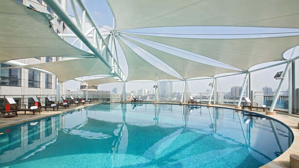 An indoor swimming pool with a modern design, surrounded by sunshades and city views. - Swissotel Foshan (Foshan)