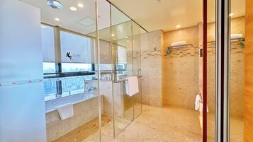 A modern bathroom with a glass shower enclosure, a sink with a towel rack, and a view of the city through a large window.