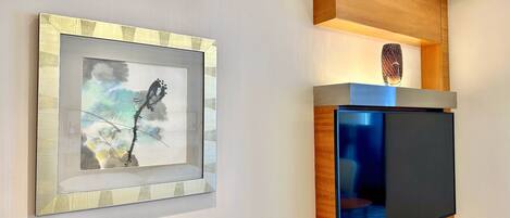 A framed artwork on a wall, a television on a wooden stand, and a shelf with a decorative item.