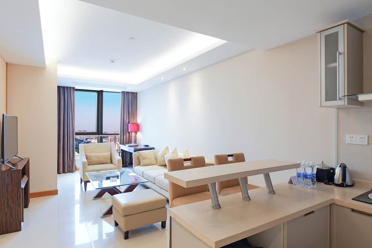 Habitación de hotel moderna con zona de comedor, sofá, televisor y vistas a la ciudad.