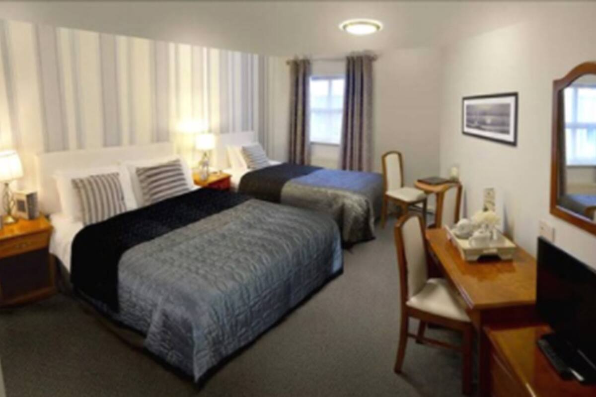 Ein Hotelzimmer mit zwei Betten, einem Schreibtisch mit Stuhl, einer Lampe und einem Bild an der Wand.