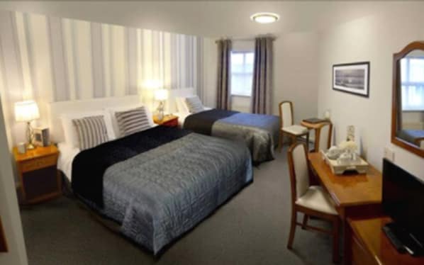 Hotellihuone, jossa on kaksi sänkyä, työpöytä tuolilla, lamppu ja taulu seinällä.