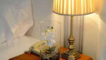 Ein Nachttisch aus Holz mit einer Lampe, einer Glaskaraffe mit einem Orchidee und einem Buch.
