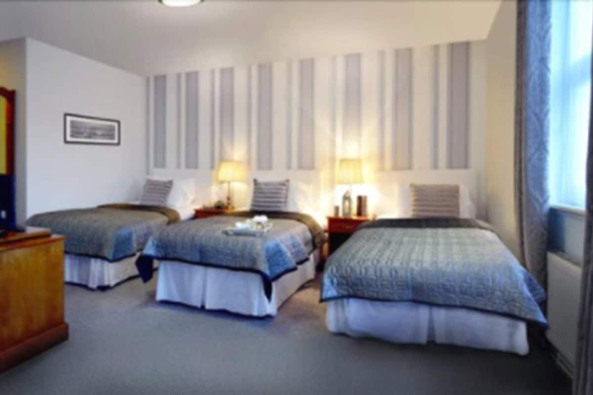 Ein Hotelzimmer mit zwei Betten, einem Nachttisch, einer Lampe und einem Fenster mit Vorhängen.