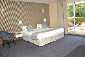Una habitación de hotel moderna con una cama grande, una mesita de noche, una silla y vistas al exterior.