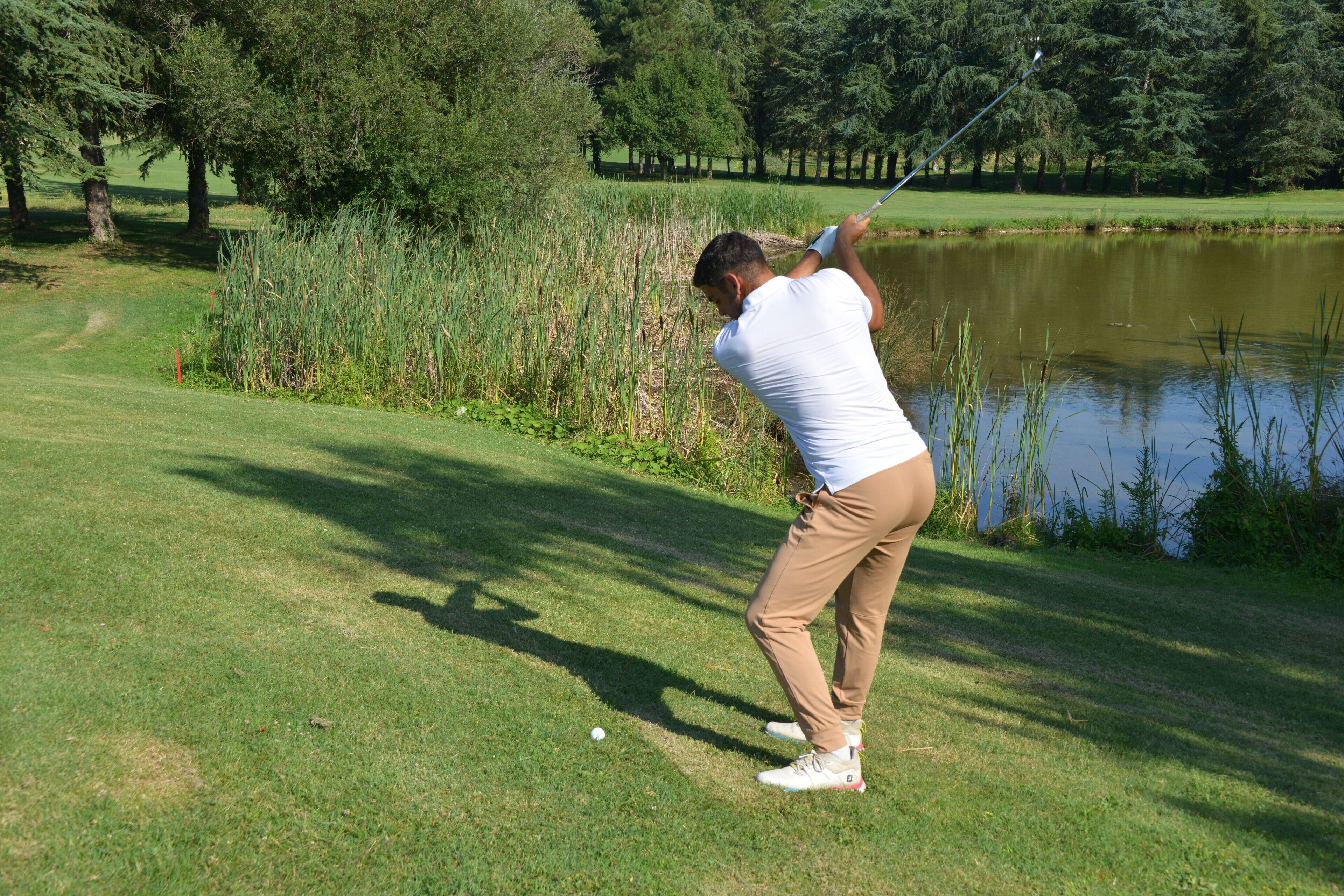 A golf course with a pond, trees, and a clear sky.