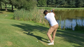 A golf course with a pond, trees, and a clear sky.
