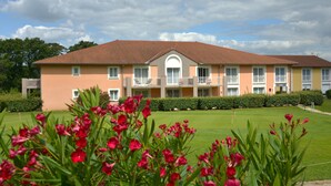 A multi-story hotel with a red-tiled roof, balconies, and a well-maintained lawn. - Domaine Golf Albon (Albon)