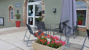 A reception area with a sign, a glass door, outdoor seating with chairs and a table, and potted plants. - Domaine Golf Albon (Albon)