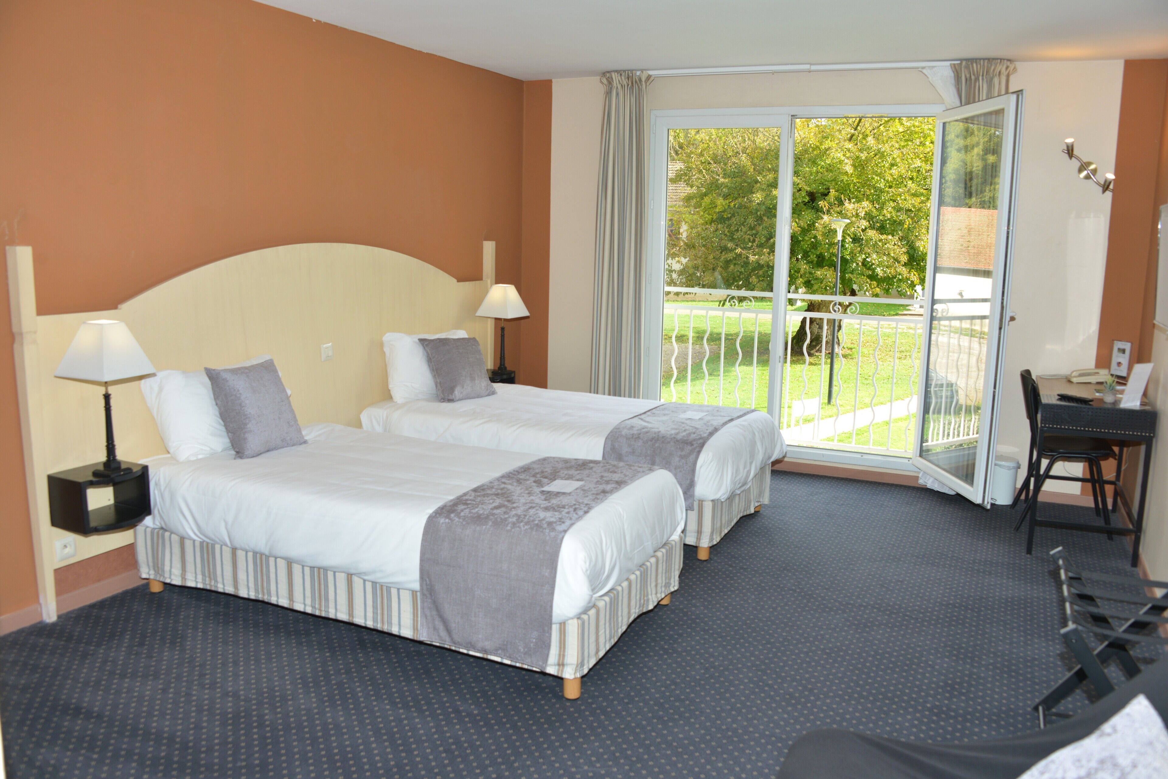 A hotel room with two beds, a balcony, a desk, and a chair.