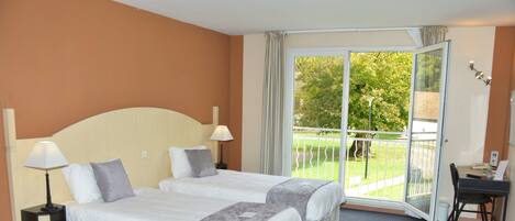A hotel room with two beds, a balcony, a desk, and a chair.