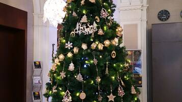 Un árbol de Navidad adornado con adornos y luces, situado en una habitación con una araña y un reloj en la pared.
