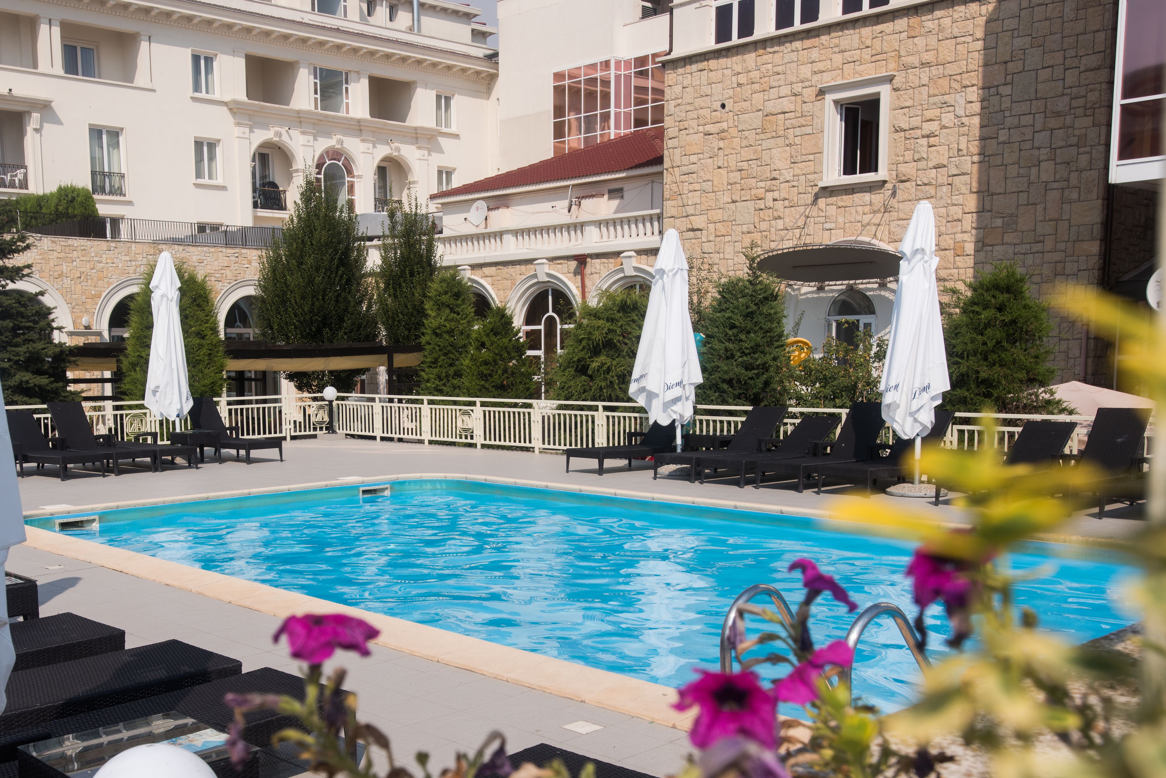 A swimming pool with lounge chairs and umbrellas, surrounded by a stone building with arched windows and balconies.