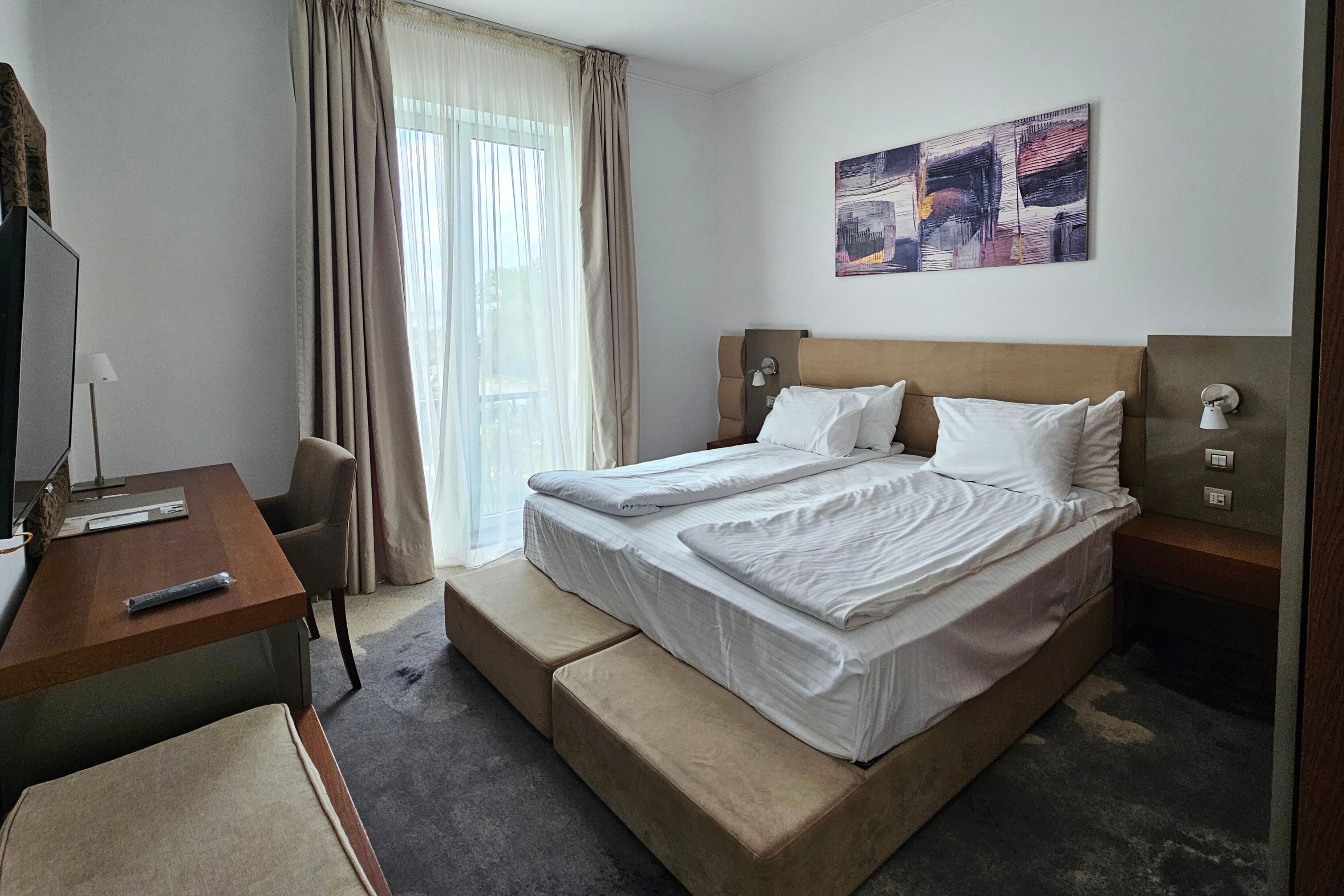 Une chambre d’hôtel avec un lit, un bureau, une chaise, une télévision et un tableau au mur.