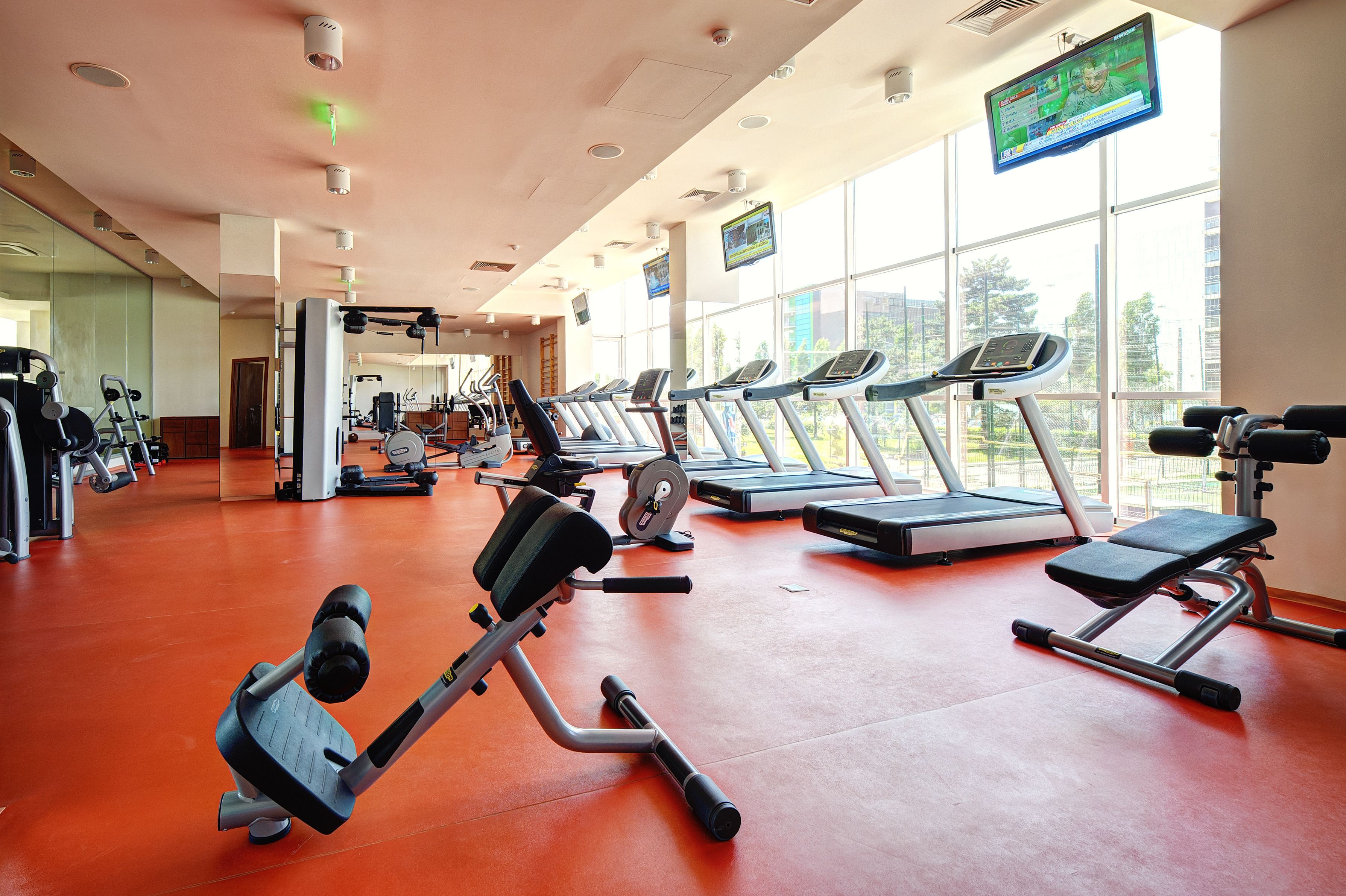 A gym with treadmills, weight machines, and a large window with a view of buildings.