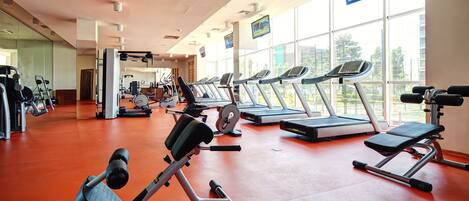 A gym with treadmills, weight machines, and a large window with a view of buildings.