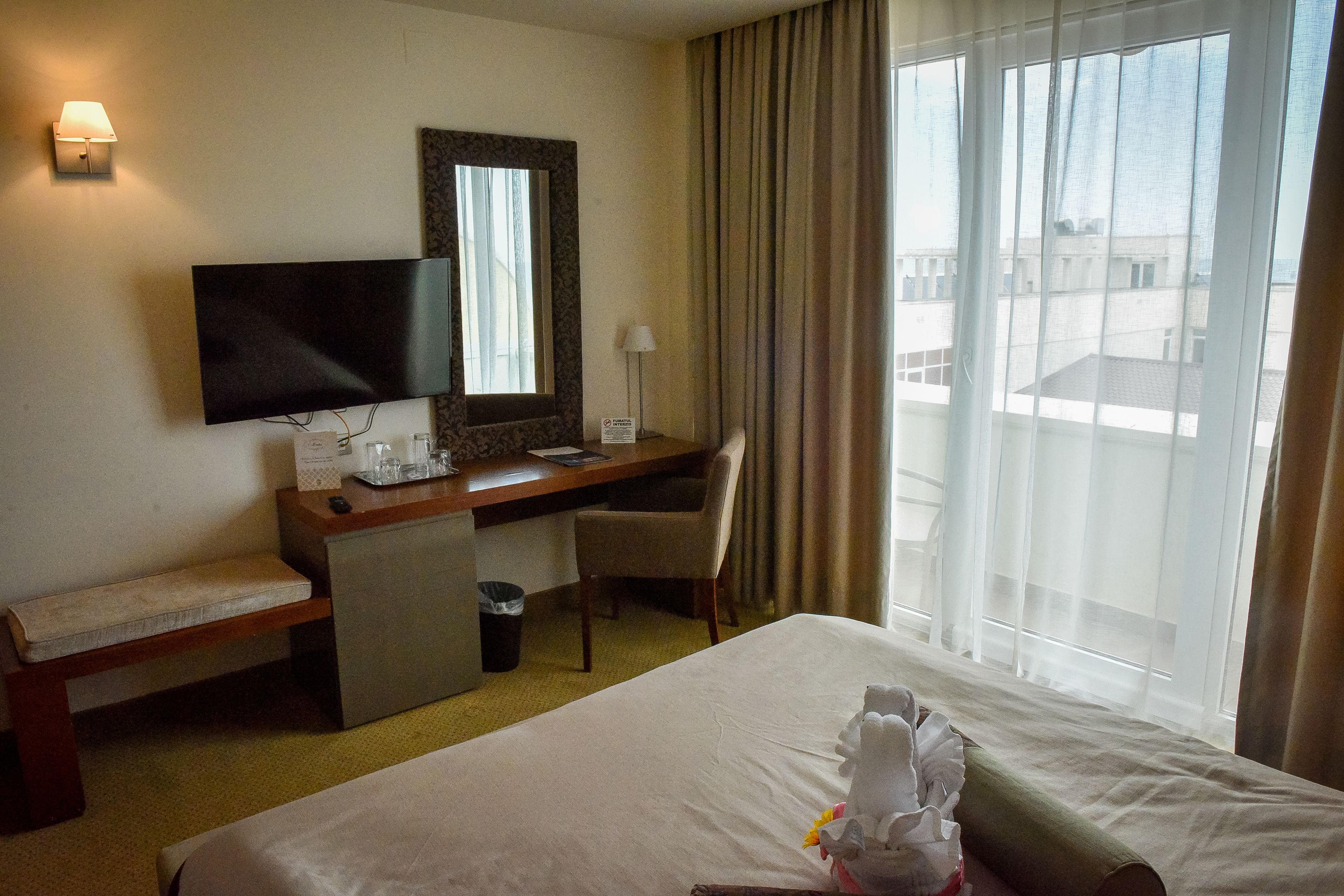 A hotel room with a bed, a desk, a chair, a TV, and a window with curtains.
