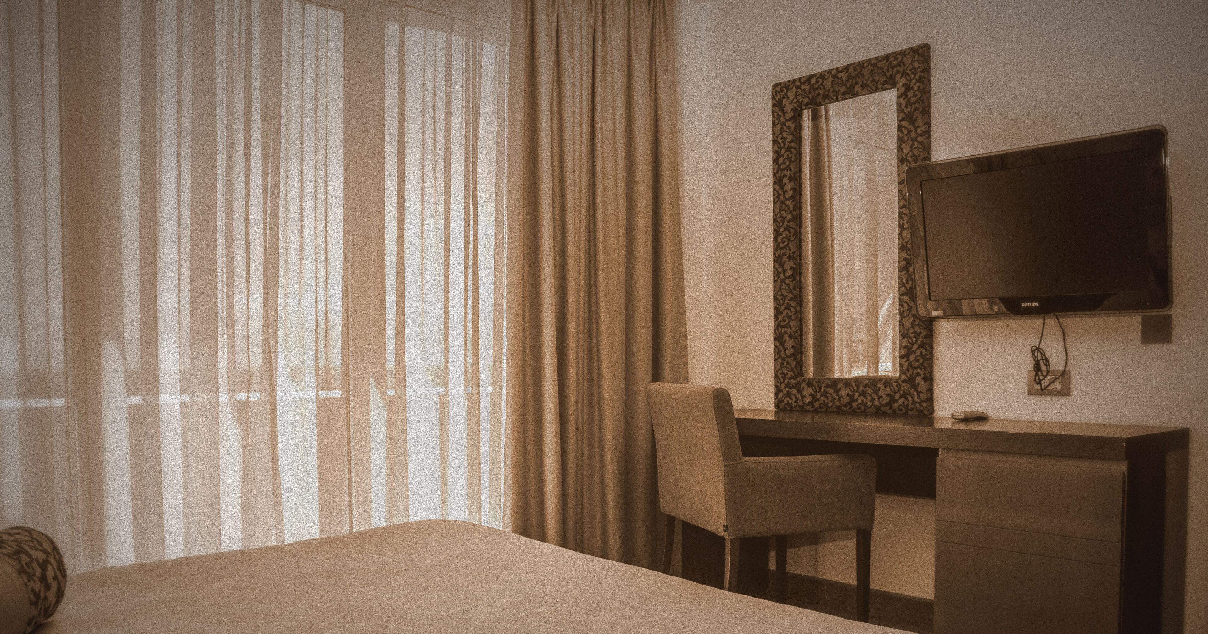 A hotel room with a bed, a desk, a chair, a television, and a large window with curtains.