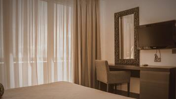 A hotel room with a bed, a desk, a chair, a television, and a large window with curtains.