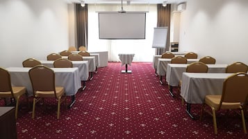 A conference room with rows of tables and chairs, a projector screen, and a carpeted floor.