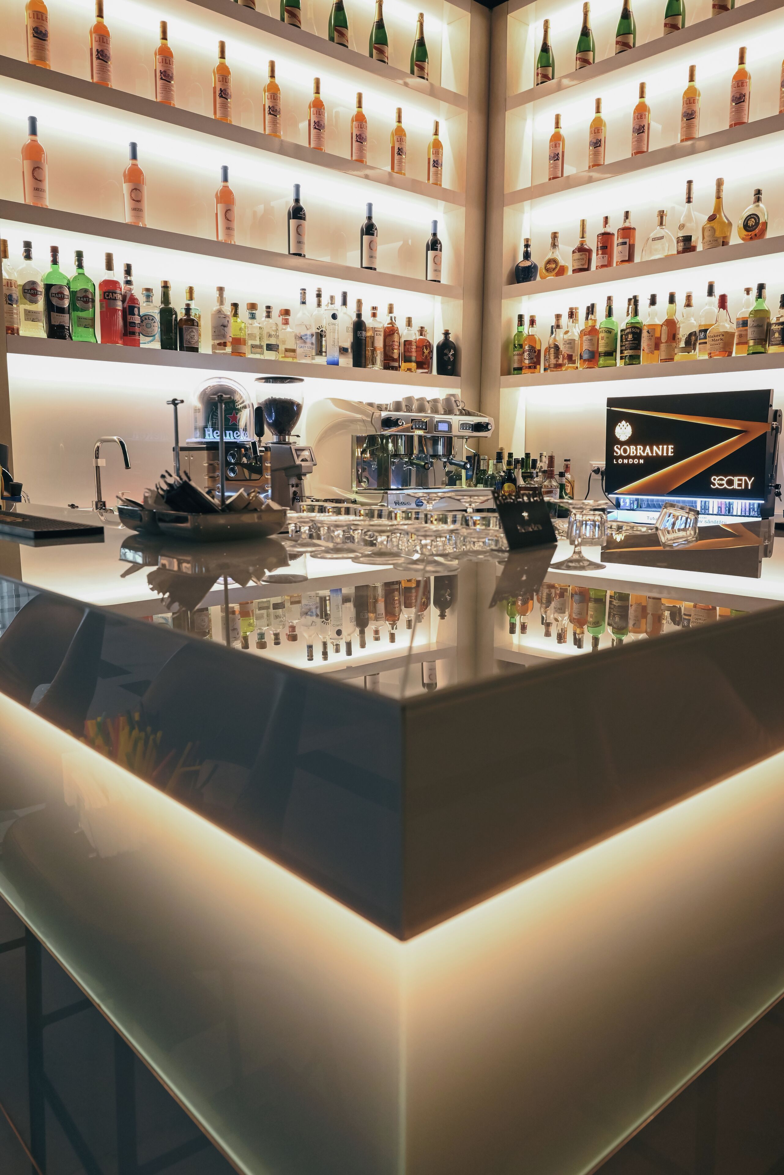 Baarialue, jossa on hyllyjä täynnä erilaisia alkoholijuomia, baaritiski ja esillä Sobranie London -pulloja.