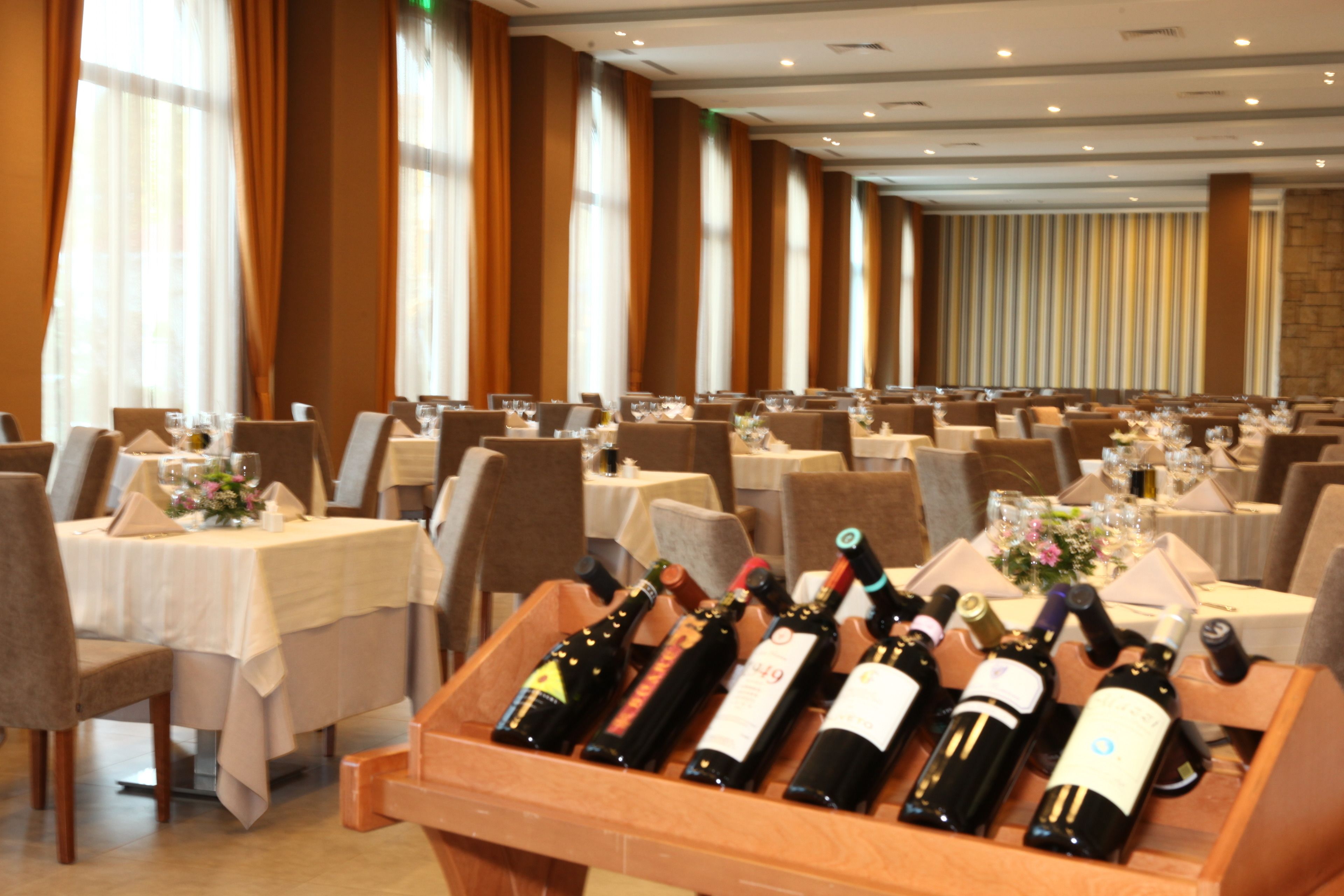 Une salle de banquet avec de nombreuses tables dressées pour le repas, chacune étant recouverte d’une nappe blanche et agrémentée de bouteilles de vin au centre.