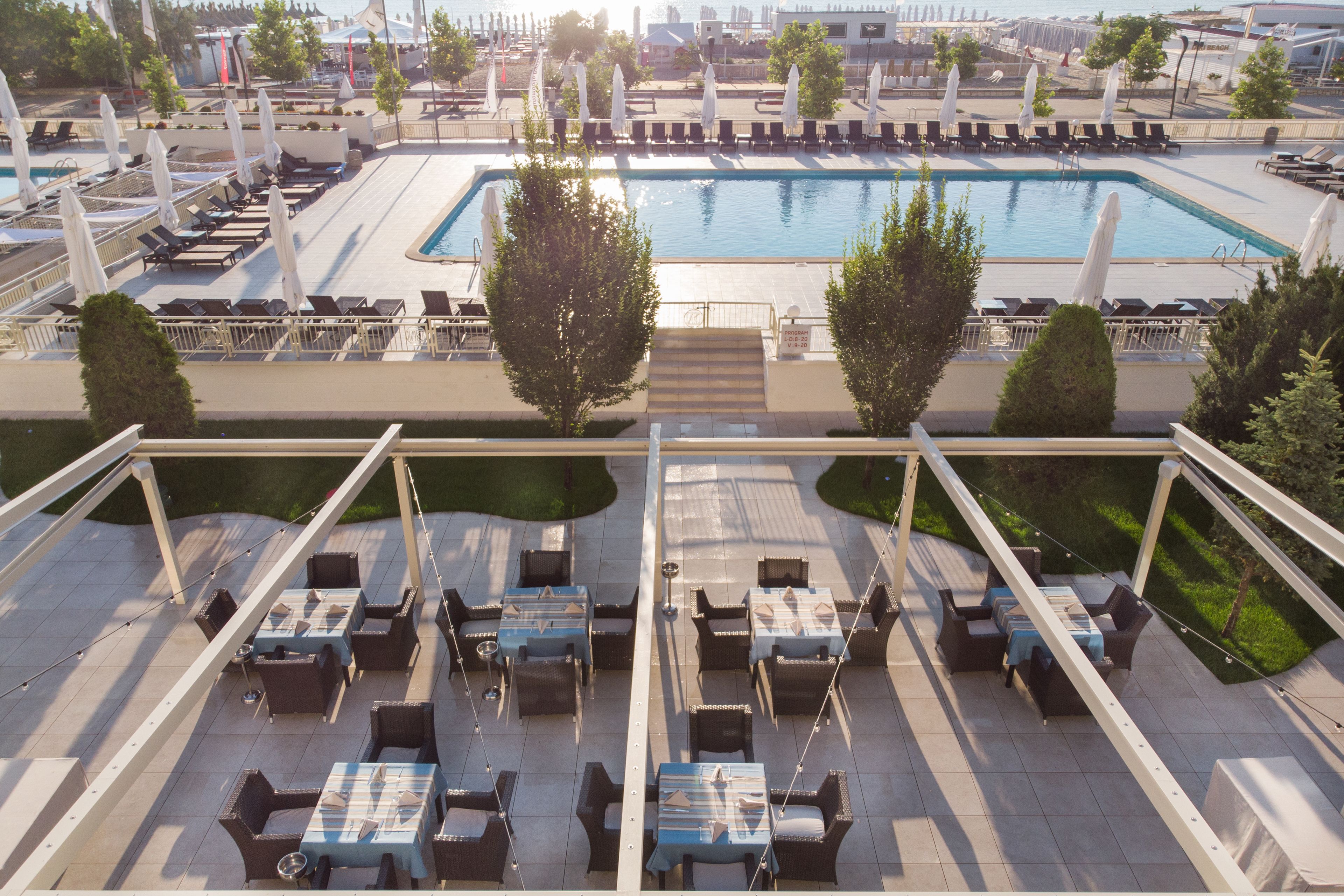 Un área de piscina en la azotea con sillones y mesas, rodeada de árboles y sombrillas.