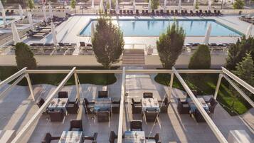 Un área de piscina en la azotea con sillones y mesas, rodeada de árboles y sombrillas.