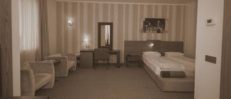 Habitación de hotel con cama, escritorio, silla y sofá. La habitación tiene papel tapiz a rayas y una lámpara de techo.