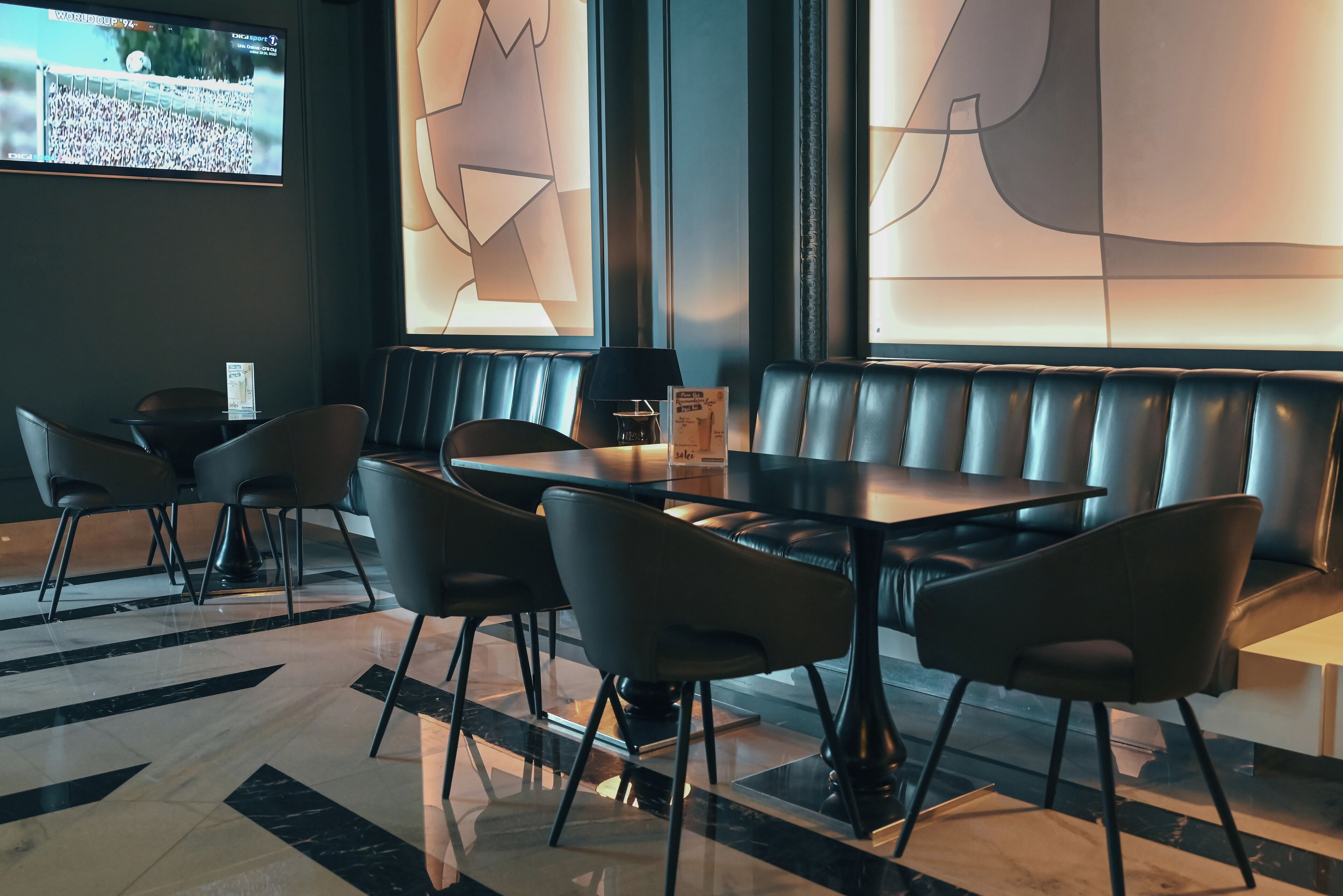 A modern restaurant with a black leather booth seating area, a glass table, and black chairs.