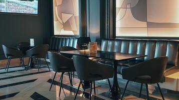 A modern restaurant with a black leather booth seating area, a glass table, and black chairs.