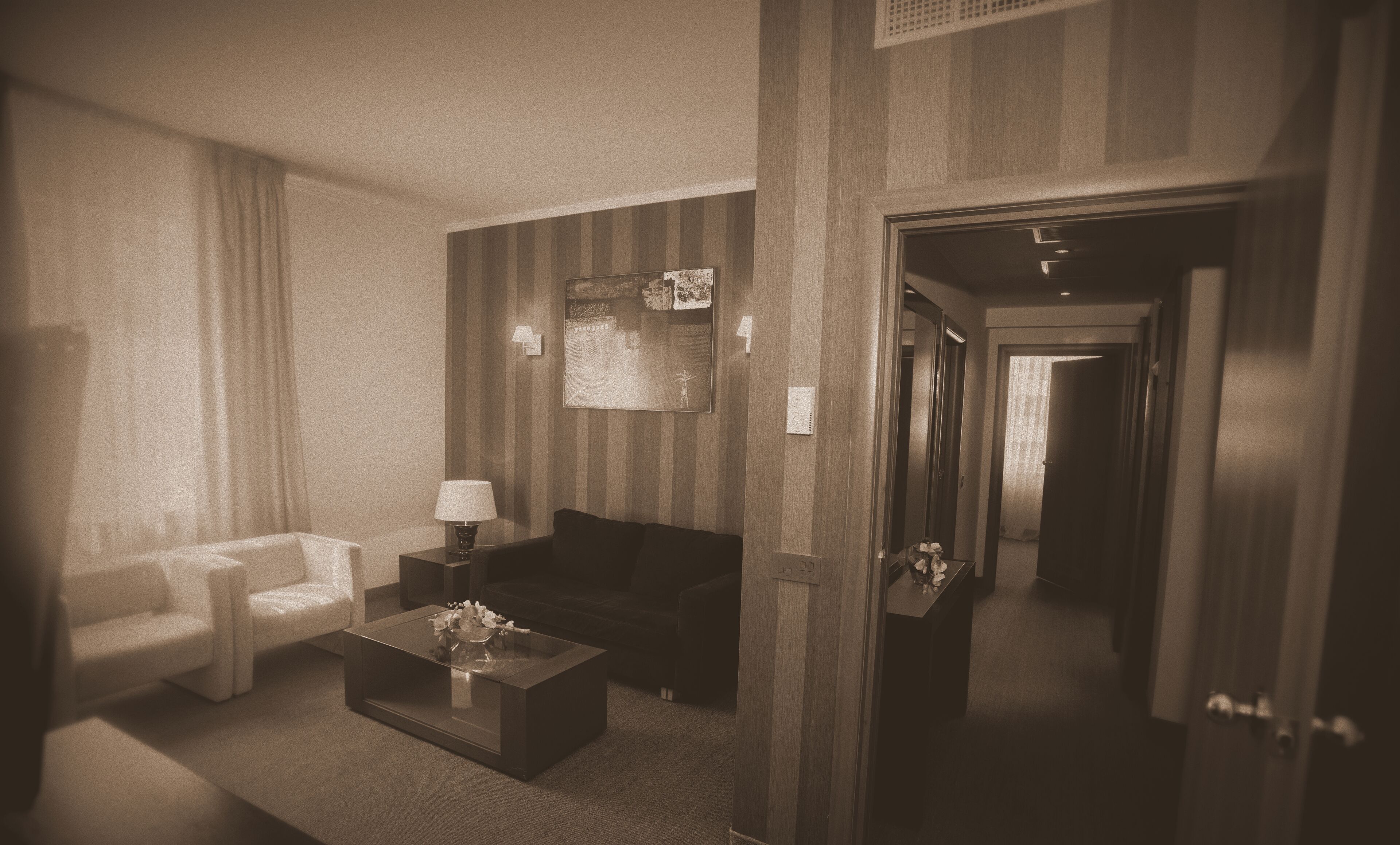 Habitación de hotel con sala de estar que incluye un sofá, un sillón y una mesita de centro. Hay un cuadro en la pared y una puerta que conduce a otra habitación.