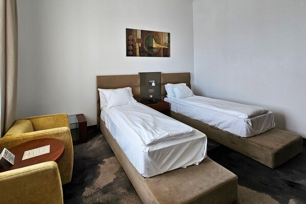 Una habitación de hotel con dos camas individuales, un pequeño sofá, una mesa y una obra de arte colgada en la pared.
