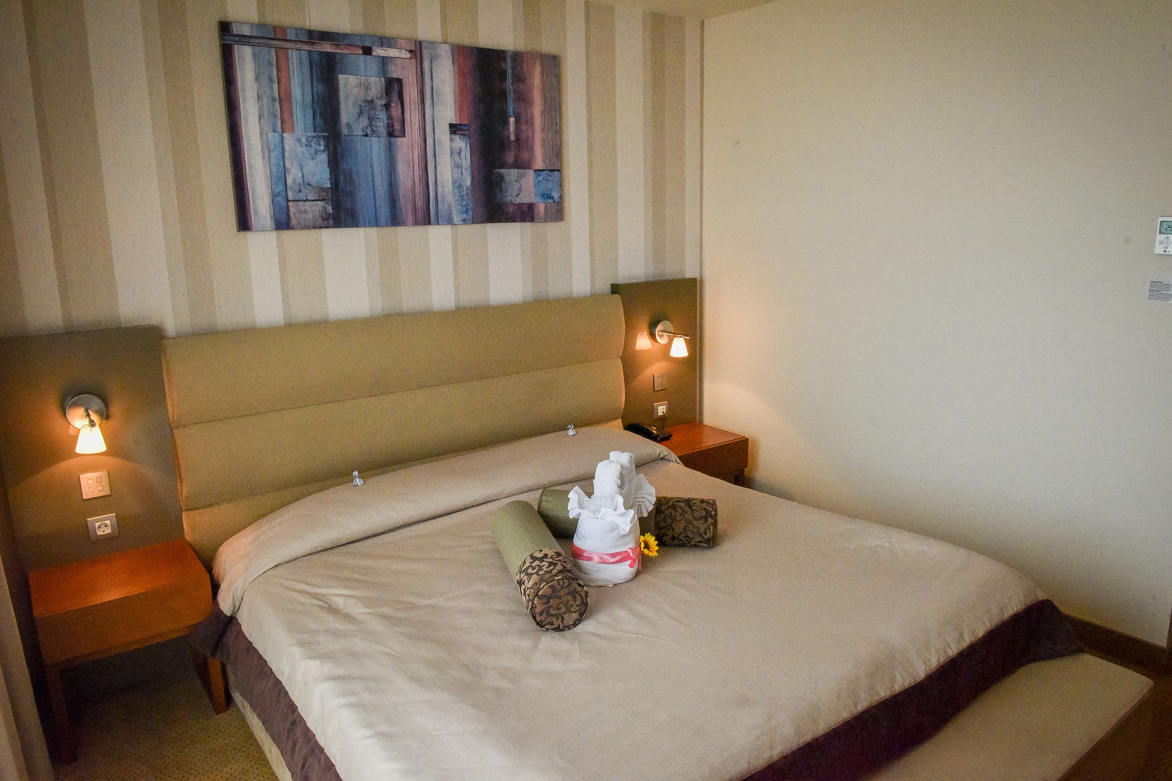 Habitación de hotel con una cama grande, dos mesitas de noche, una obra de arte en la pared y una mesilla con lámpara.