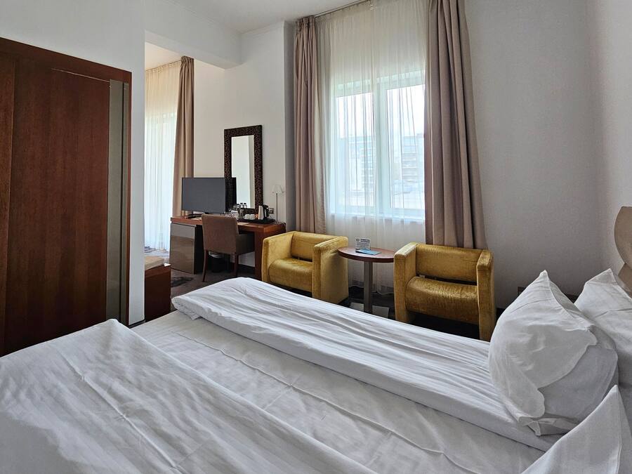 Una habitación de hotel con una cama, dos sillas, un escritorio con una computadora y un espejo grande.