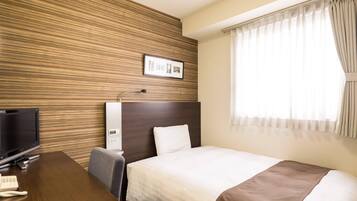 Ett hotellrum med en väggpanel i trä, en säng med ett vitt och brunt överkast, ett skrivbord med en tv och en telefon samt ett fönster med gardiner.