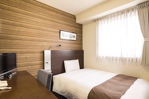 Quarto de hotel com painel de parede de madeira, cama com colcha branca e marrom, escrivaninha com televisão e telefone, e janela com cortinas.