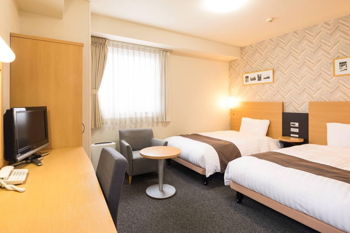 Habitación de hotel con dos camas, un escritorio con teléfono, una silla, una mesita redonda y una televisión.