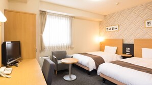 Une chambre d’hôtel avec deux lits, un bureau avec un téléphone, une chaise, une petite table ronde et un téléviseur.